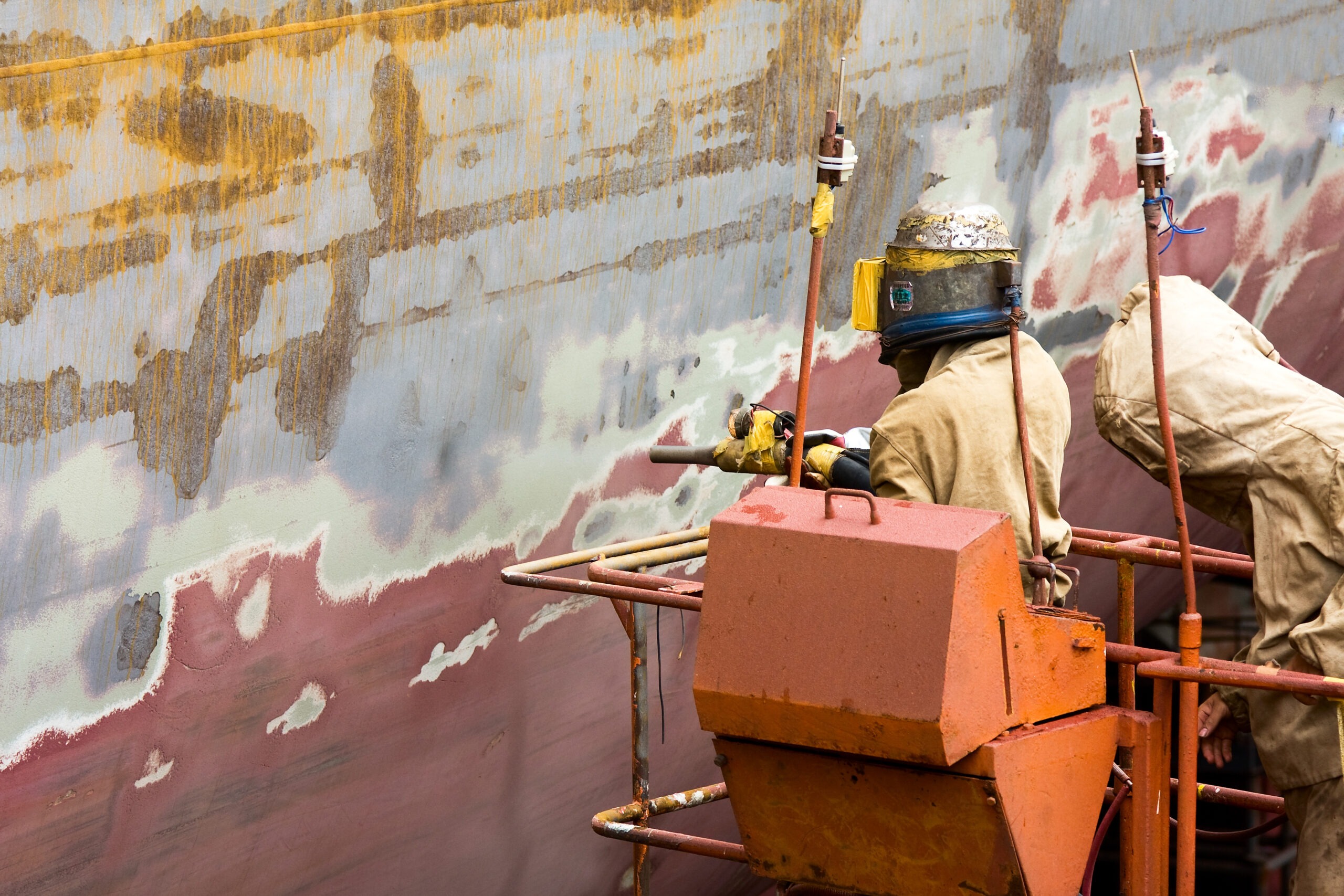 Workers in protective gear sand a large ship's hull