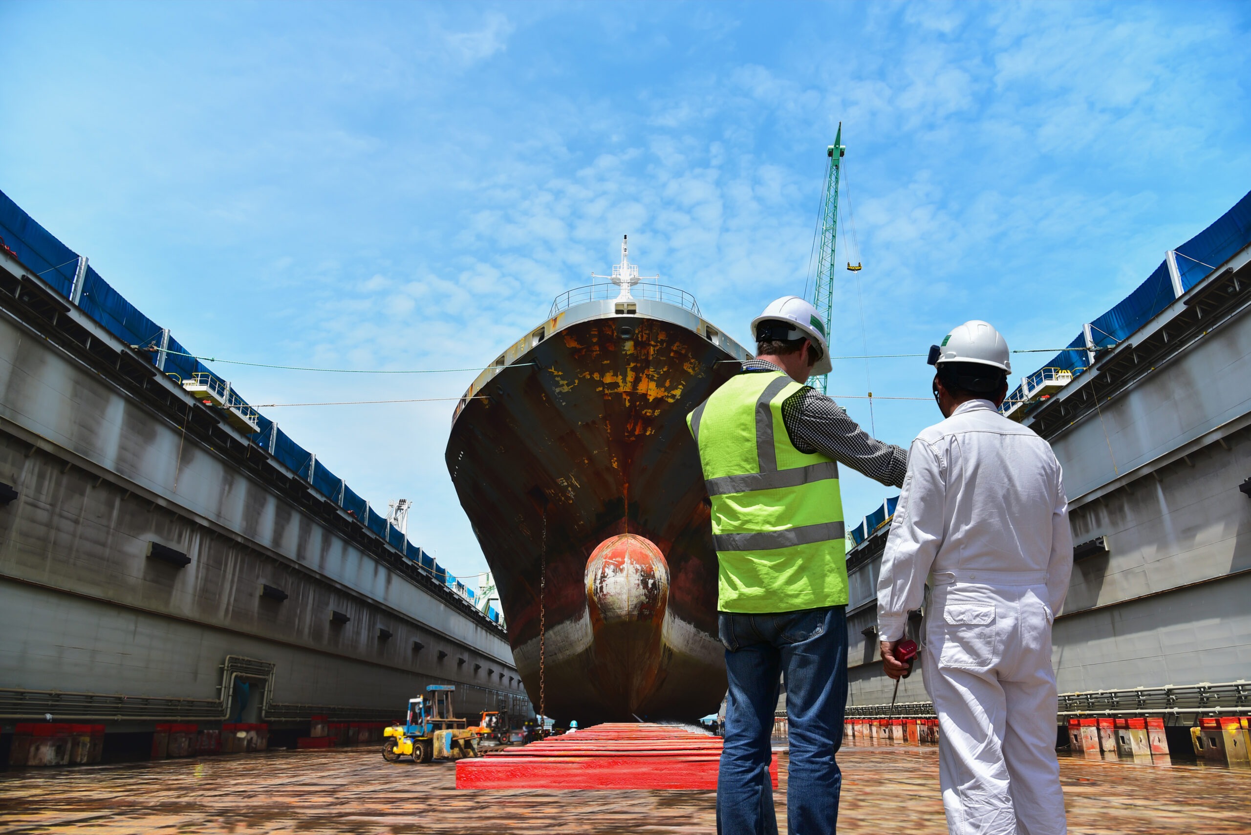 Workers in safety gear inspect a large ship in dry dock